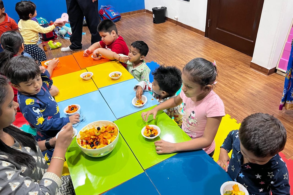 Children at Elzee Preschool participating in a summer camp fruit salad making session, mixing colourful fruits in small bowls.