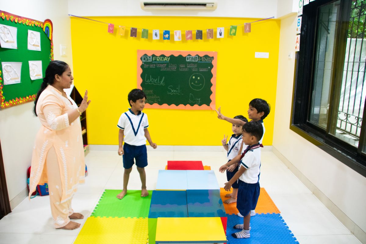 A preschool teacher guiding a group of young children during an interactive classroom activity at Elzee Preschool, with kids standing on colorful floor mats and participating in a learning game.